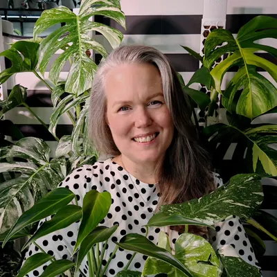 Nina smiling among her variegated Monsteras in front of the striped wall